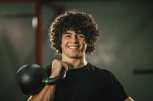 A handsome muscular man is doing hard training with kettlebell at the gym.