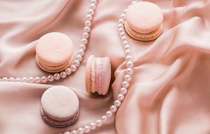 Girly, bakery and branding concept - Sweet macaroons and pearls jewellery on silk background, parisian chic jewelry, French dessert food and cake macaron for luxury confectionery brand, holiday gift