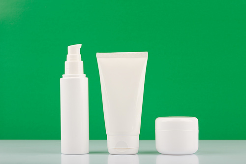 Minimalistic still life with organic cosmetic products set for smooth, firm and young looking skin and daily beauty routine on white glossy table against green background.