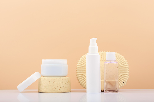 Set of beauty products, white opened jar on podium and tube with cream and lotion against beige background with copy space. Concept of natural skin care