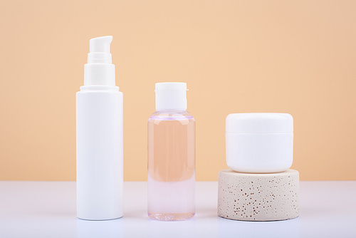 Minimalistic still life with set of cosmetic bottles with face cream, lotion and lip balm on white table against beige background. Concept of healthcare and beauty