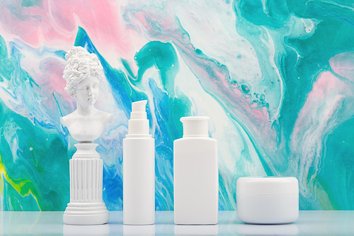 Set of cosmetic products with gypsum woman figure against blue marbled background. Concept of skin care and beauty treatment