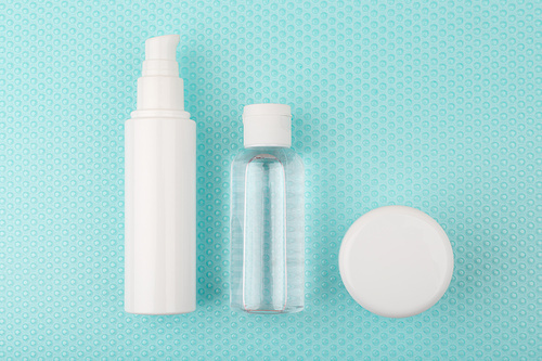 Toiletries on light blue background with bubbles. Moisturizing cream, exfoliating lotion and under eye cream set for daily skin care routine