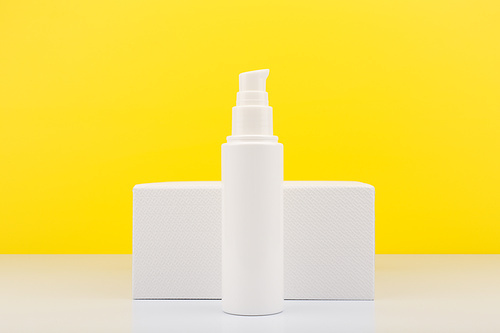 Face moisturizing cream or lotion in tall white tube against white geometric podium and yellow background with copy space. Concept of skin moisturizing and protective treatment with Spf for summer