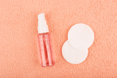 CLEAR SPRAY BOTTLE AND COTTON PADS ON PEACH  COLOR BACKGROUND MINIMALIST SKINCARE ESSENTIALS.