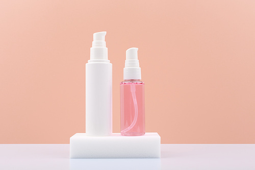 Cosmetic tubes with face cream and pink gel or foam for skin cleaning or exfoliating on white pedestal against pink background with copy space