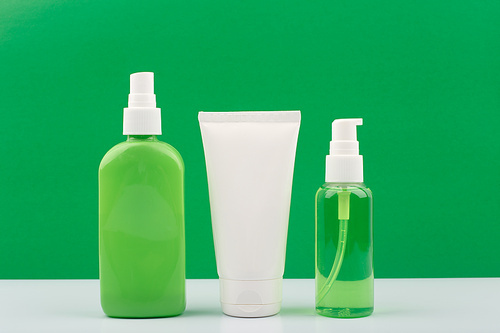 Set of green and white cosmetic bottles against yellow background. Concept of organic beauty products with natural ingredients. Moisturizing body spray, face cream and cleansing gel for face.