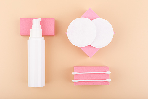 Creative flat lay with make up removing product, cotton pads and cotton swabs on pink podiums against beige background. Concept of skin care and make up removing