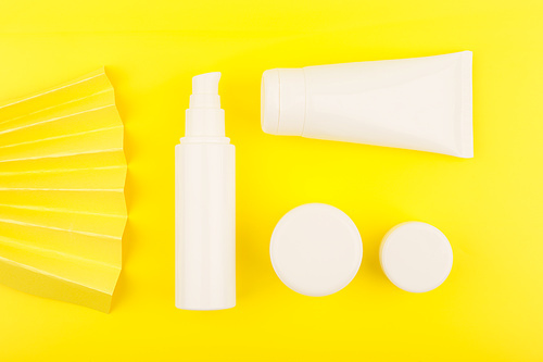 Creative flat lay with cosmetic products for skin care in white unbranded tubes on yellow background decorated with yellow waver. Concept of skin care and beauty treatment