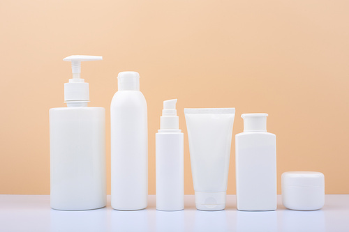 Set of white unbranded cosmetic bottles for face and body care in a row against bright beige background. Concept of organic, natural, eco friendly cosmetics and beauty products