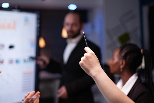 Selective focus of businesswoman leder sitting at desk analyzing marketing presentation discussing financial graps paperwork. Diverse multi-ethnic teamwork brainstorming project ideas working in meeting room late night