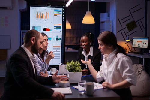 Diverse multi-ethnic businesspeople analyzing management strategy working overtime in company office meeting room late at night. Overworked leader overworking marketing strategy in evening