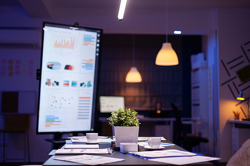 Modern empty business corporate office meeting room is ready for businesspeople late at night. In background on conference table standing company financial documents with economy graphs