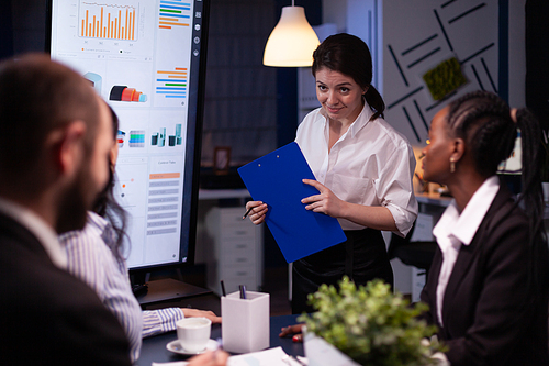 Focused multi ethnic businesspeople working in company meeting office room brainstorming management strategy late at night. Entrepreneur woman presenting business financial ideas.