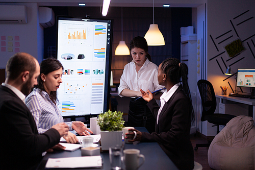 Workaholic entrepreneur woman discussing management statistics overworking in office meeting room late at night. Diverse multi-ethnic businesspeople solving company ideas in evening