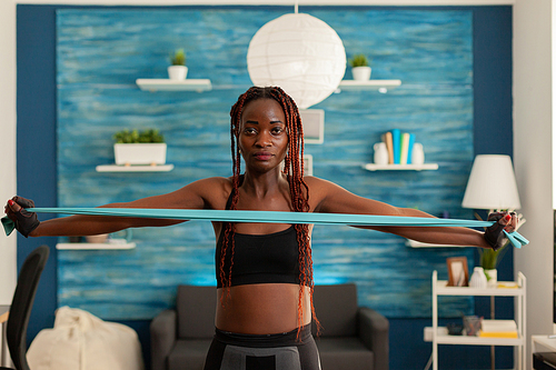 Black woman exercising muscle strength with rubber band in home living room for healthy body. African stretching resistance band during intense workout training.