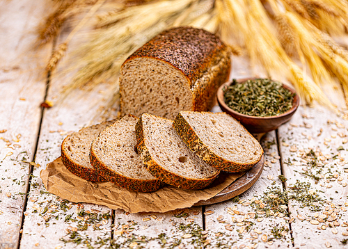 Loaf of bread with dried basil on wooden background