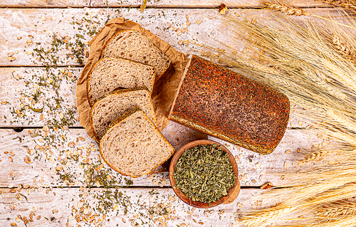 Flat lay of loaf of bread with dried basil on wooden background