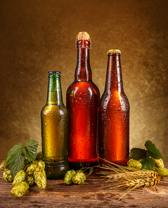 Beer bottles with wheat and hops on wooden table