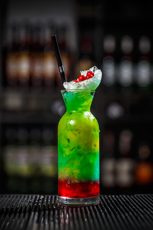 Fancy multicolored cocktail with drinking straw served on the bar counter