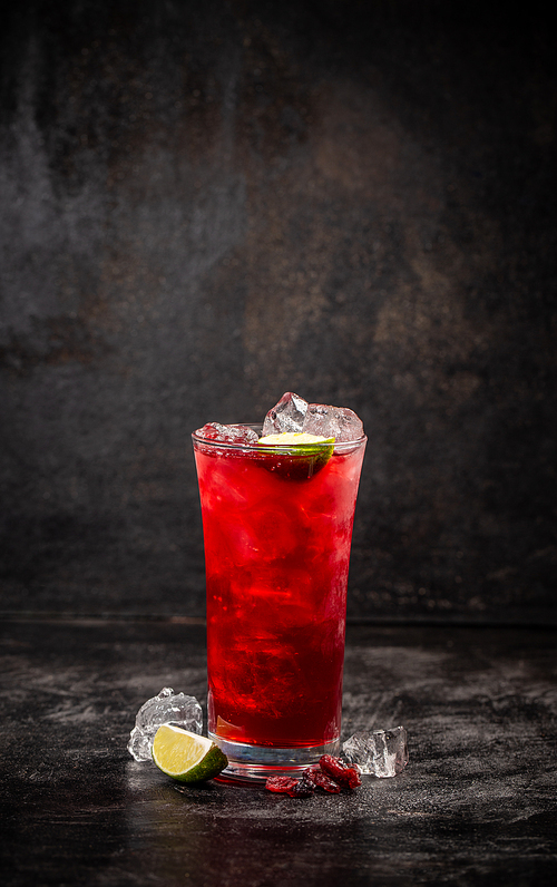 Refreshment alcoholic red cranberry and lime cocktail with ice on dark background, copy space