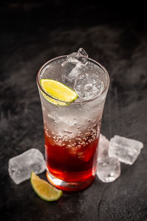 Soda drink with strawberry syrup and ice cubes decorated with lime wedge