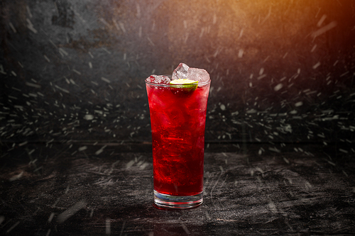 Cranberry beverage with ice and lime on dark background