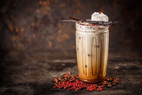 Iced coffee with milk in tall glass spiced with pink peppercorn and vanilla