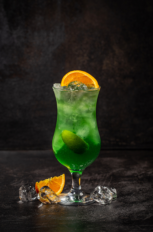 Green apple fruit alcohol cocktail decorated with orange wedge on dark background