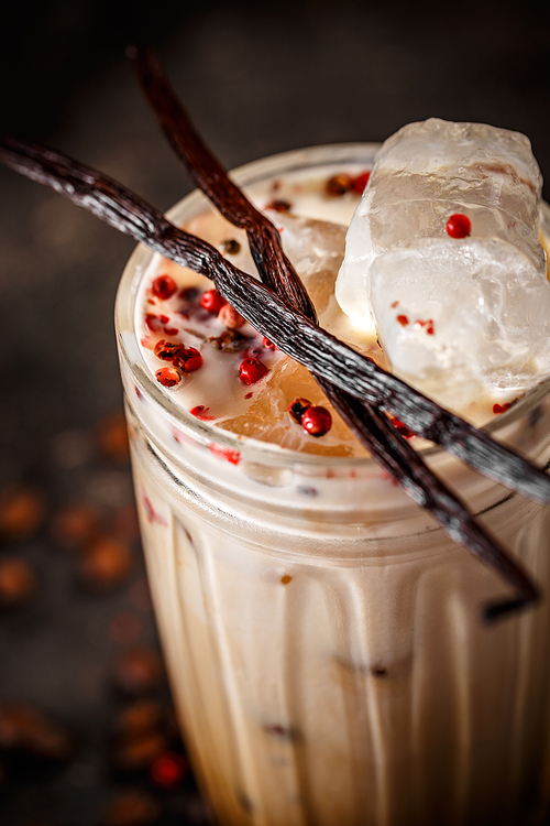 Close up of tall glass iced coffee latte with pink peppercorn and vanilla