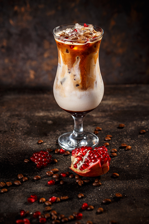 Glass of cold tasty pomegranate coffee latte on vintage dark background