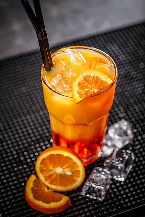 Glass of fresh orange cocktail with ice cube and straw