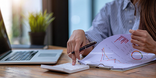 Close up Business woman using calculator and laptop for do math finance on wooden desk in office and business working background, tax, accounting, statistics and analytic research concept