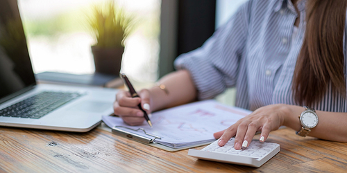 Close up Business woman using calculator and laptop for do math finance on wooden desk in office and business working background, tax, accounting, statistics and analytic research concept