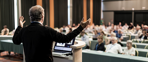 Speaker at Business Conference with Public Presentations. Audience at the conference hall. Business and Entrepreneurship concept. Rear view. Panoramic composition. Background blur.