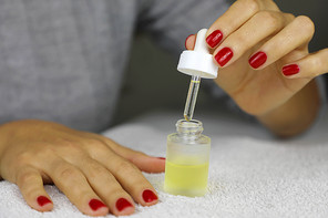 Manicure oil hand. Female hands take care of cuticles with oil. Girl with red nail polish sitting at the table and takes care of her cuticles.