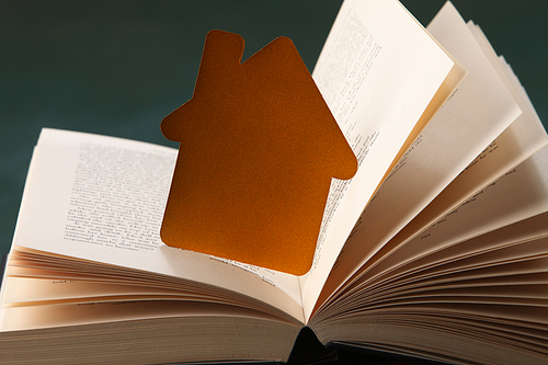 paper house on open book, sitting on green background.