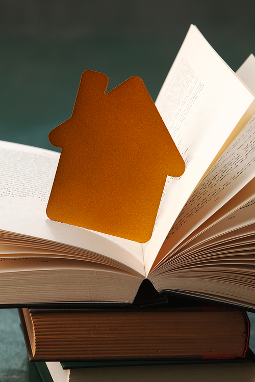 paper house on open book, sitting on green background.