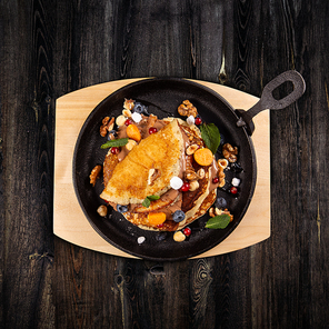 Delicious sweet pancakes served on a cooking pan with fresh fruits, nuts and chocolate sauce