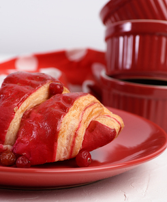 baked croissant with cherry glaze on a red ceramic plate, white table, close up