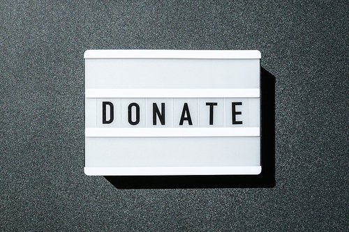 Lightbox board on a black background with the words DONATE in black letters. Money