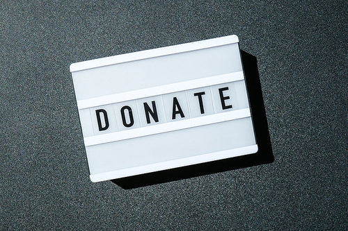 Lightbox board on a black background with the words DONATE in black letters. Money