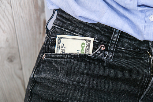 Close up hand of businesswoman holding banknote into pocket. Profitable investment. The exchange of currencies. Money to buy debt securities increase revenue. Hand puts dollar bills in the pocket jeans. The concept of giving a bribe