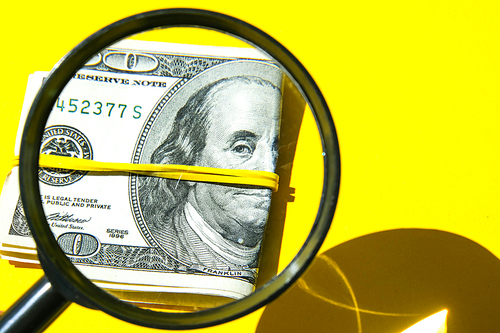 Magnifying glass on the background of a bundle of dollars close-up, one hundred dollars franklin, one thousand texture, background. Business budget of wealth and prosperity finance.