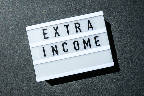 Lightbox board on a black background with the words EXTRA INCOME in black letters. Money