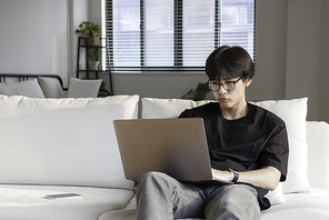 거실 소파에 앉아 노트북을 사용하면서 메일을 확인하고 있는 캐주얼 복장을 입은 매력적인 진지한 대학생 남자 청년