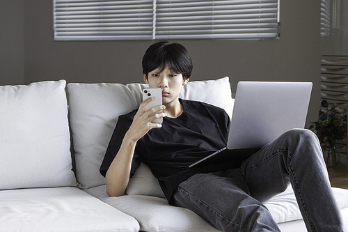 거실 실내에서 스마트폰 핸드폰 화면을 보고 온라인으로 좋은 소식이 담긴 이메일을 읽고 있는 젊은 대학생 남자 청년