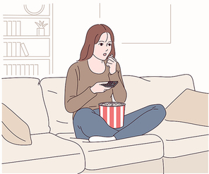 한 여성이 소파에 앉아 팝콘을 먹으며 티비를 보고 있다.