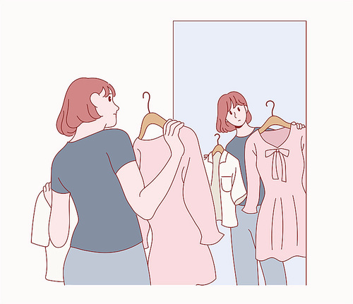 한 여성이 거울을 보며 옷을 고르고 있다.