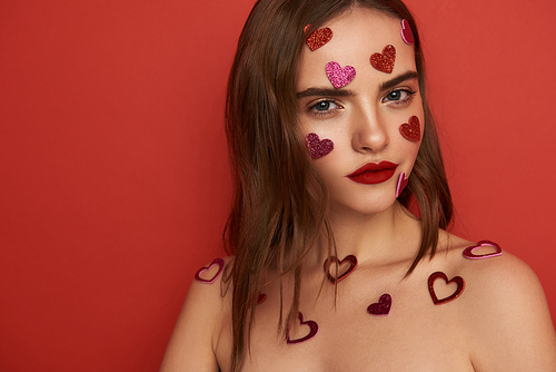 Cropped photo of charming young lady  in studio. Her face is covered with decorative glossy hearts. Close up. Love concept